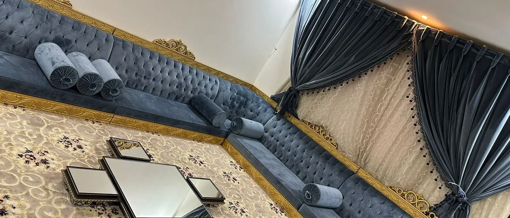 سجادة مزخرفة في مجلس بمقاعد زرقاء وستائر طويلة لحساب سعر غسيل السجاد بالمتر